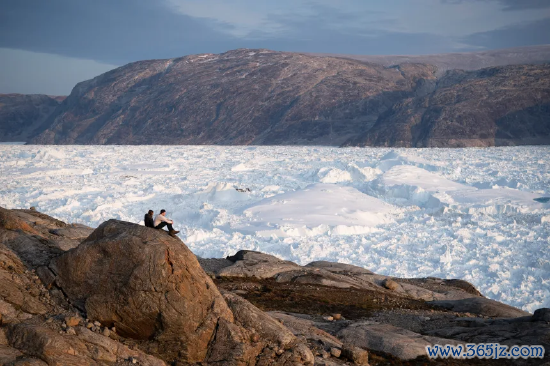 2019 年 8 月 16 日，纽约大学的学生研究员们坐在岩石上，眺望格陵兰岛的黑尔海姆冰川。